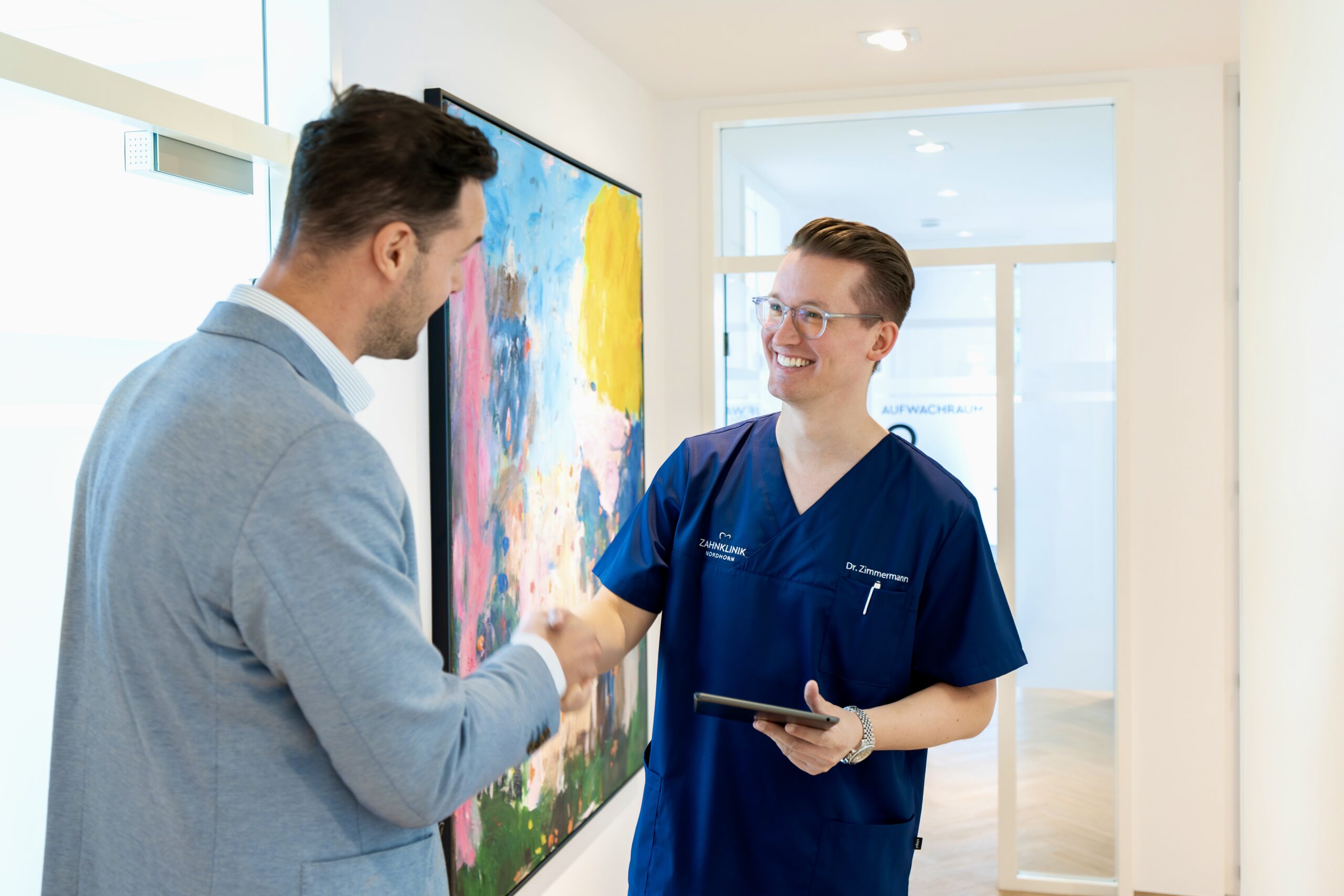 Zahnarzt der Zahnklinik Nordhorn begrüßt Patienten mit einem freundlichen Händedruck – persönliche Betreuung und vertrauensvolle Kommunikation in moderner Praxis.