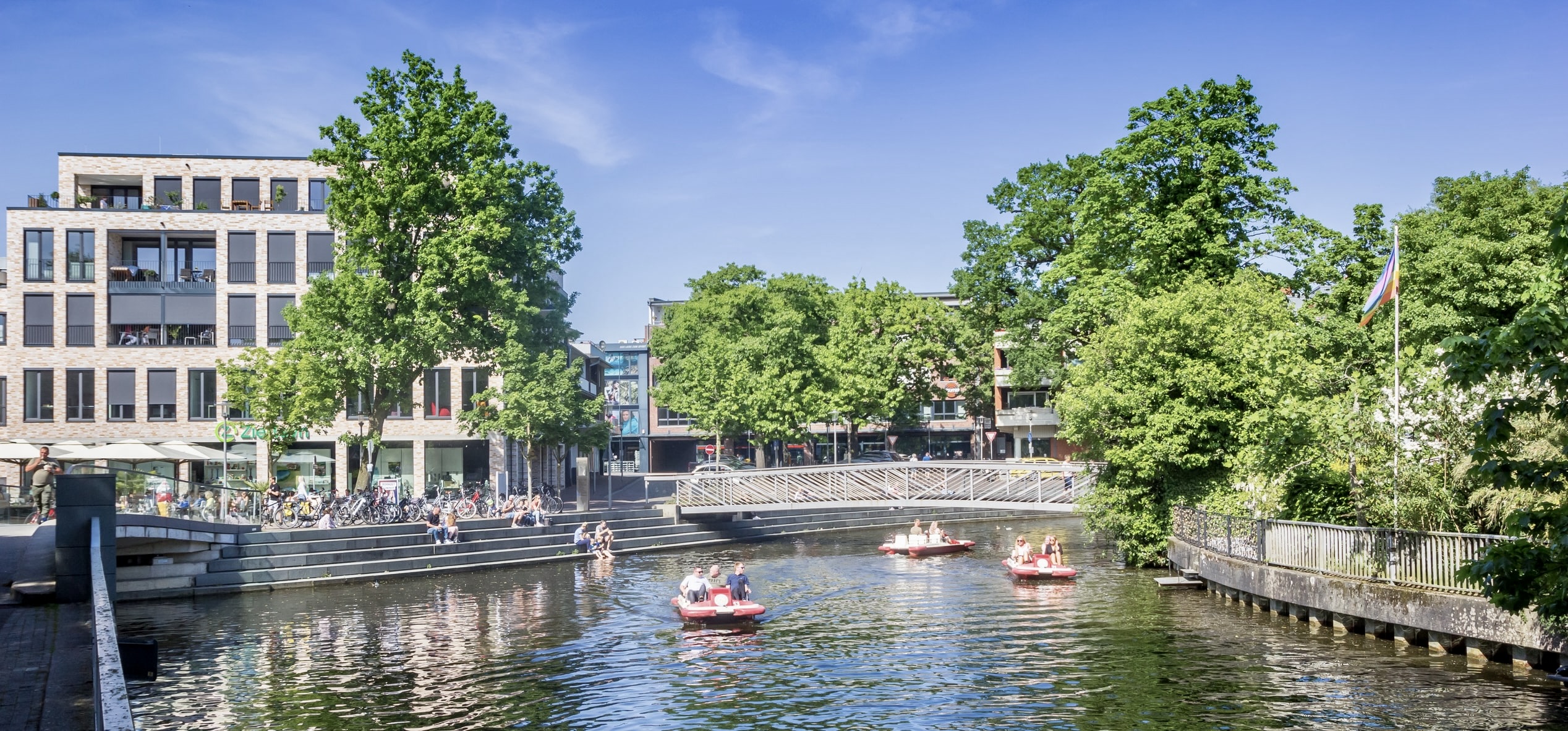 Sommerliche Ansicht der Innenstadt von Nordhorn mit Kanal, Tretbooten und moderner Architektur.